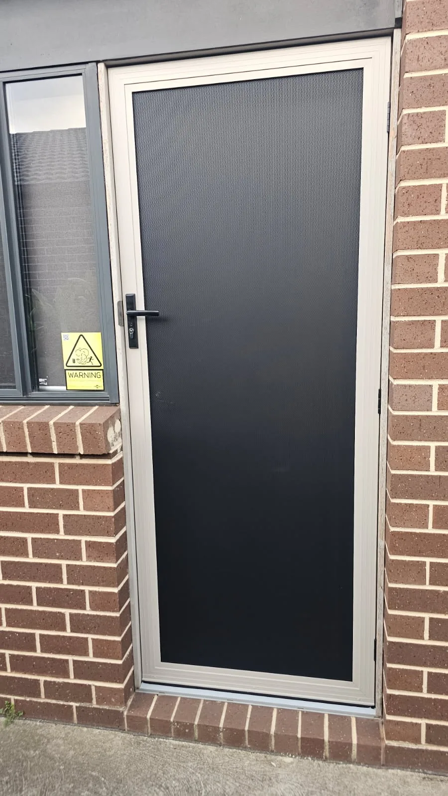 White-framed mesh security door installed at a brick home entry