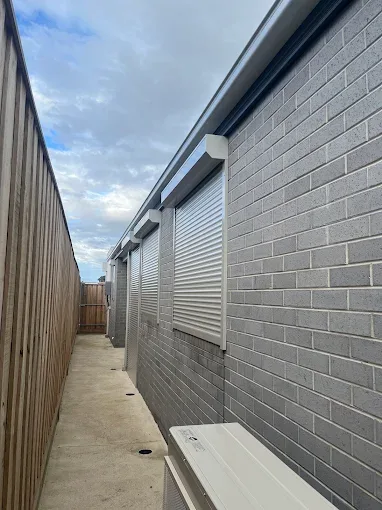 Light grey roller shutters fitted to a row of side windows on a grey brick home