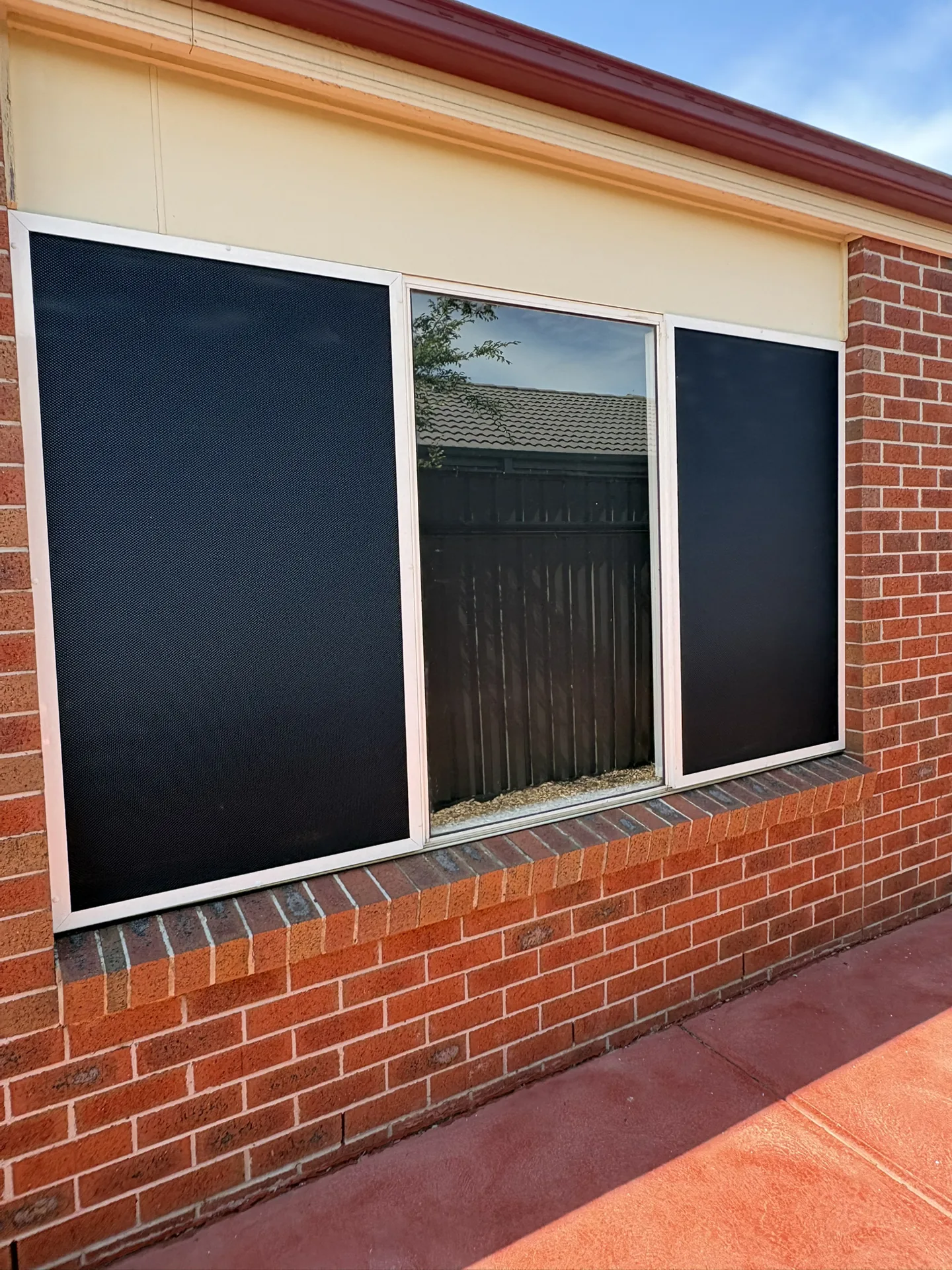 Two white-framed security screens fitted to windows on a brick home