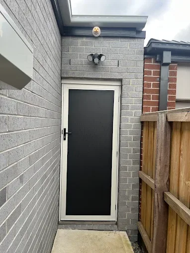 Cream-framed hinged security door with dark mesh on a brick home's side entry