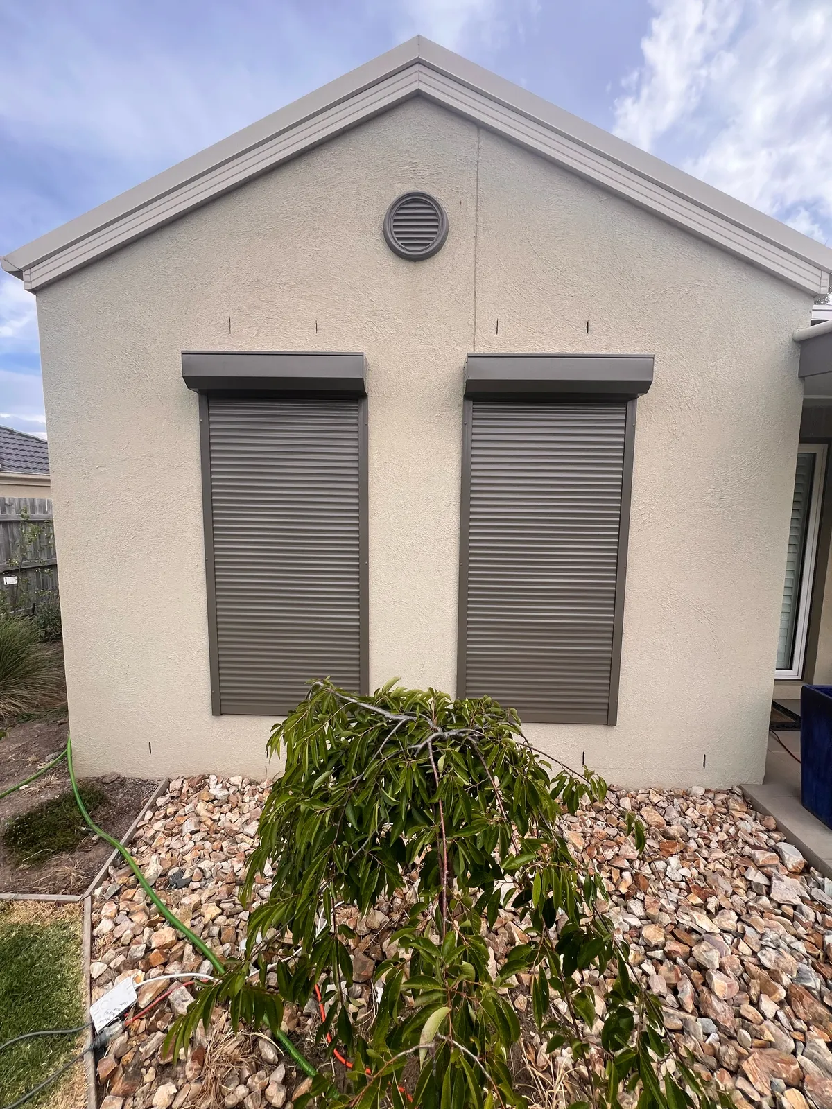 Two roller shutters on side-by-side windows below the gable of a rendered home