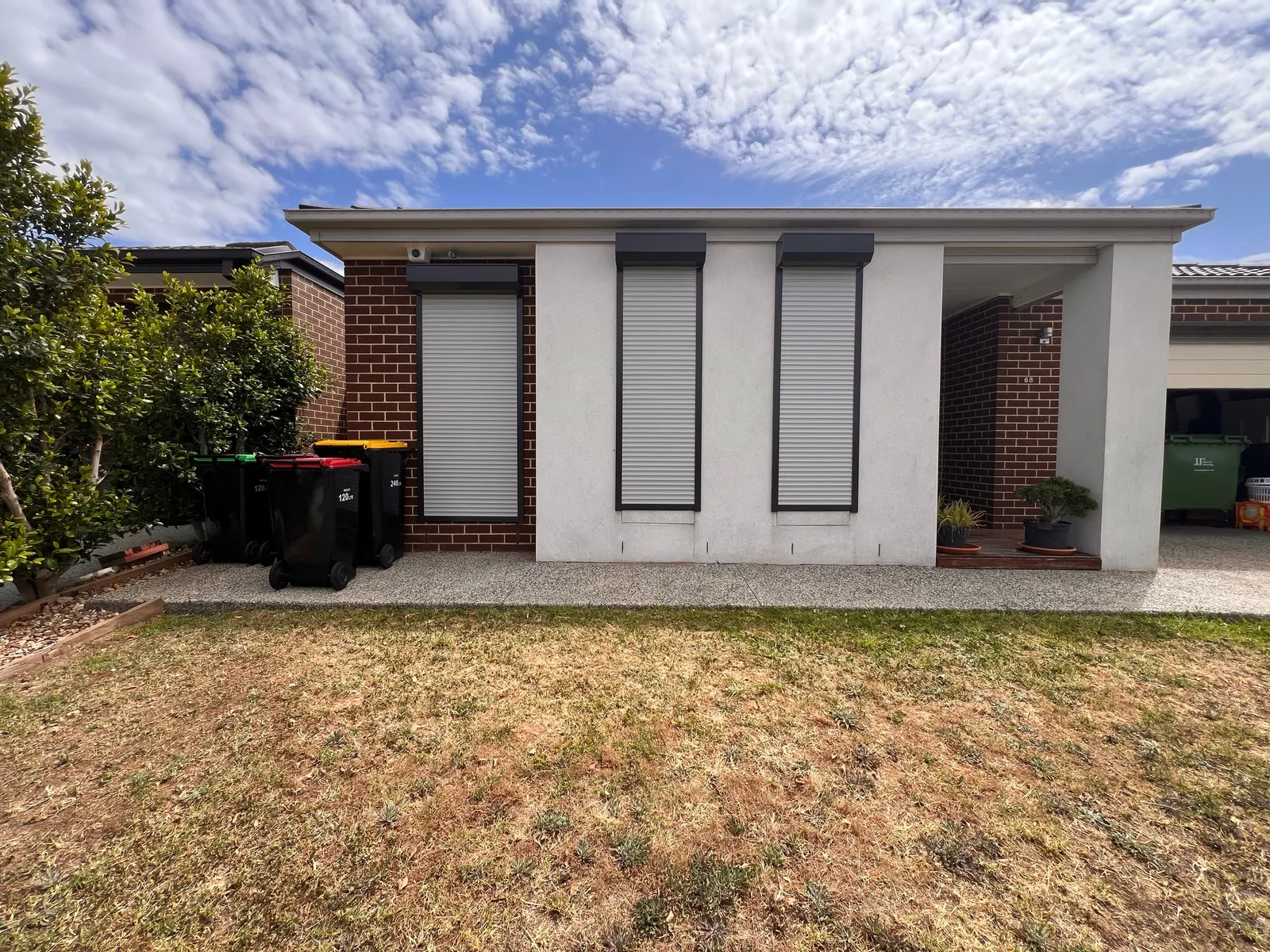Roller shutters on the front windows of a home with brick and rendered sections