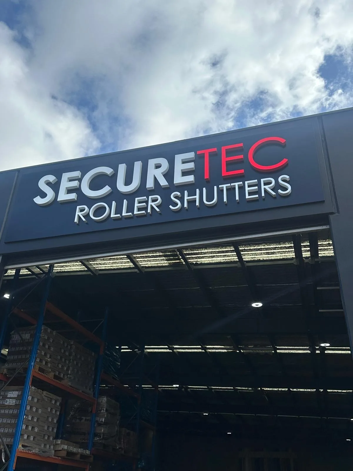 Securetec Roller Shutters sign above the open workshop door, with stock on racking inside