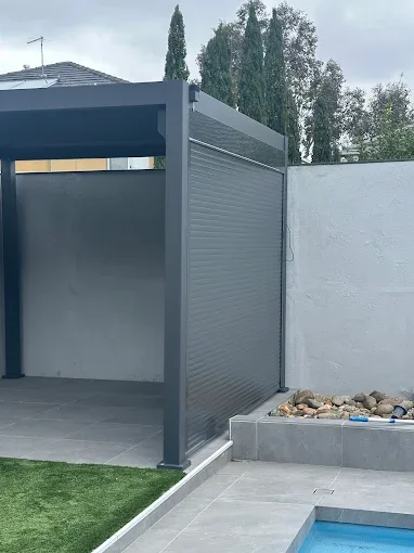 Charcoal roller shutter enclosing the side of an outdoor pergola area next to a pool