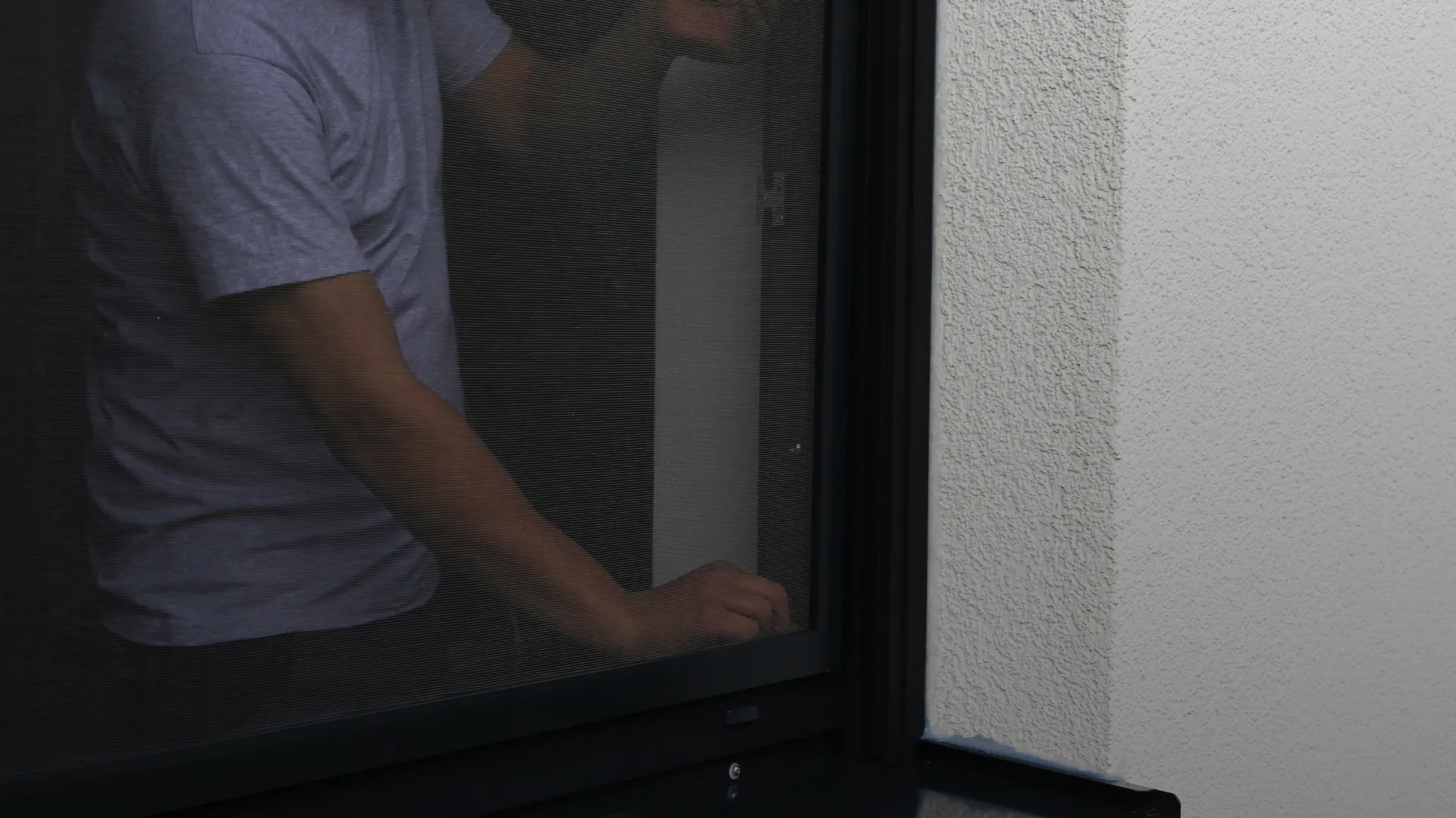 Person behind a dark-framed fly screen fitted to a rendered window opening