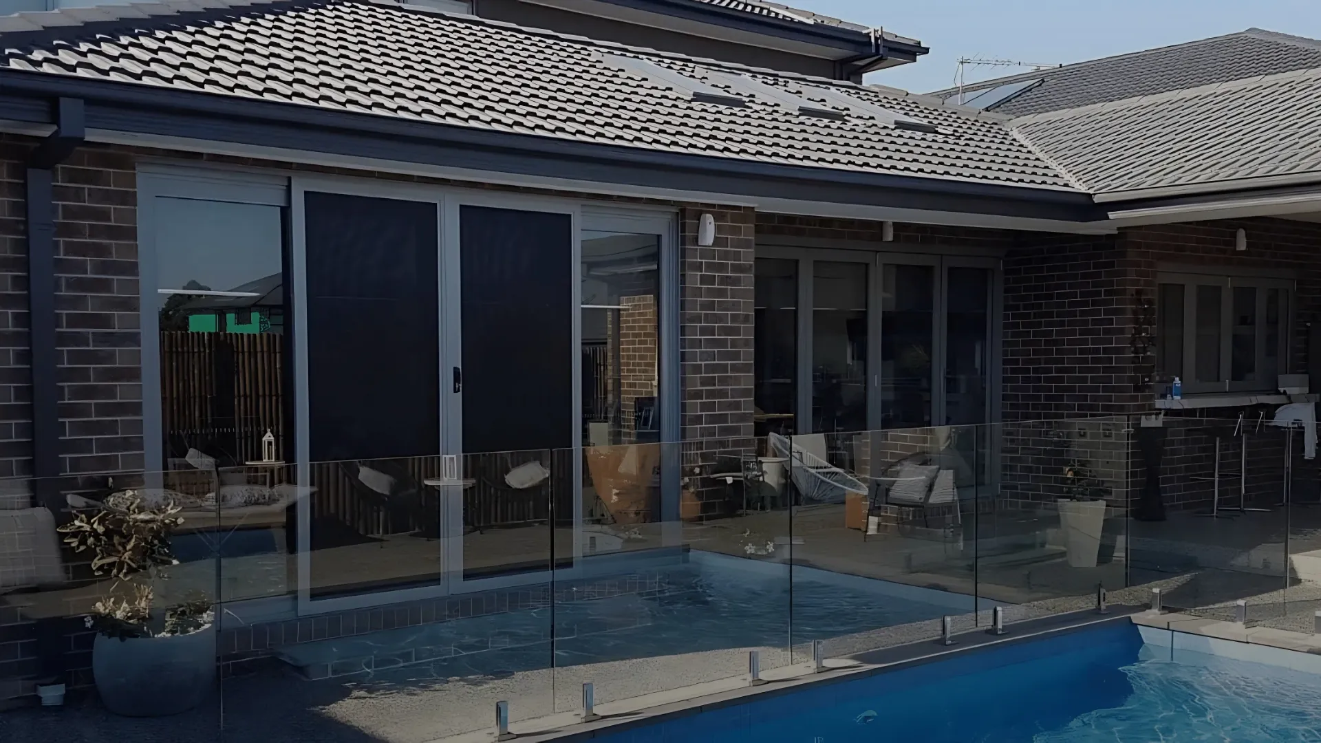 Black mesh sliding security doors on a brick home beside a fenced pool