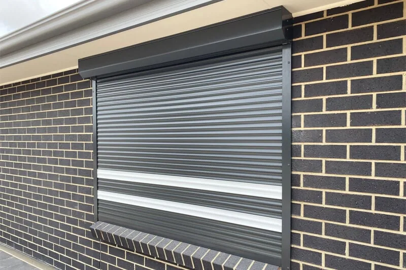 Charcoal roller shutter lowered over a window on a dark brick wall