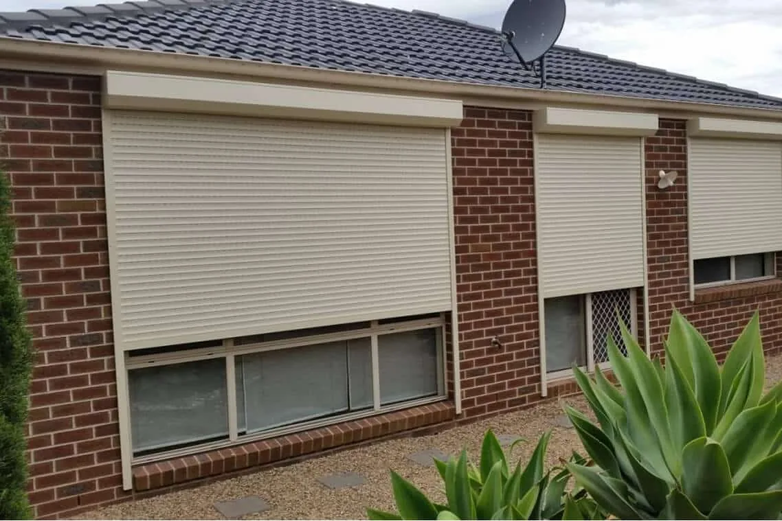 Multiple roller shutters installed across windows of a brick home