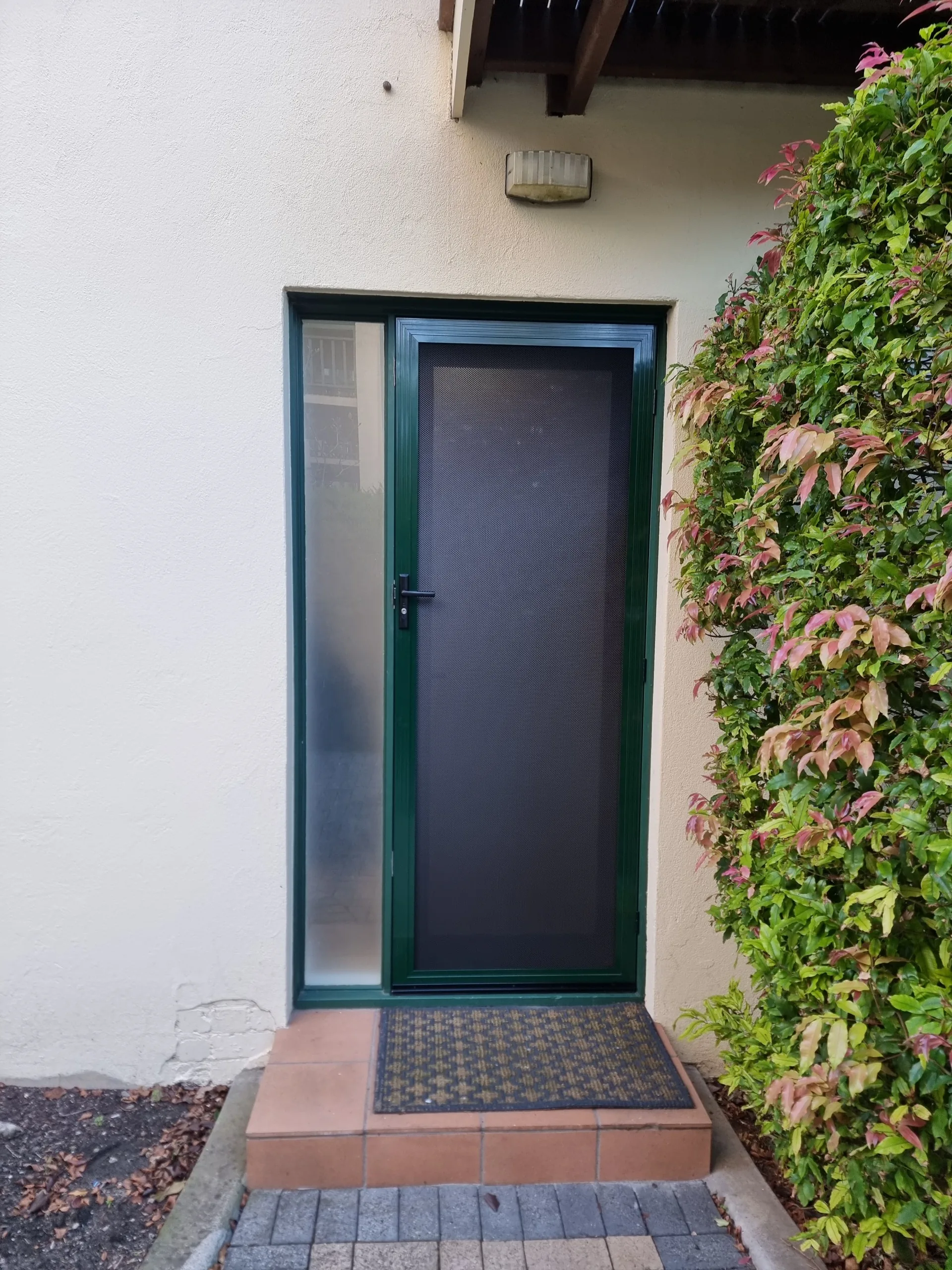 Green hinged security door with a matching sidelight installed at the entry of a brick home
