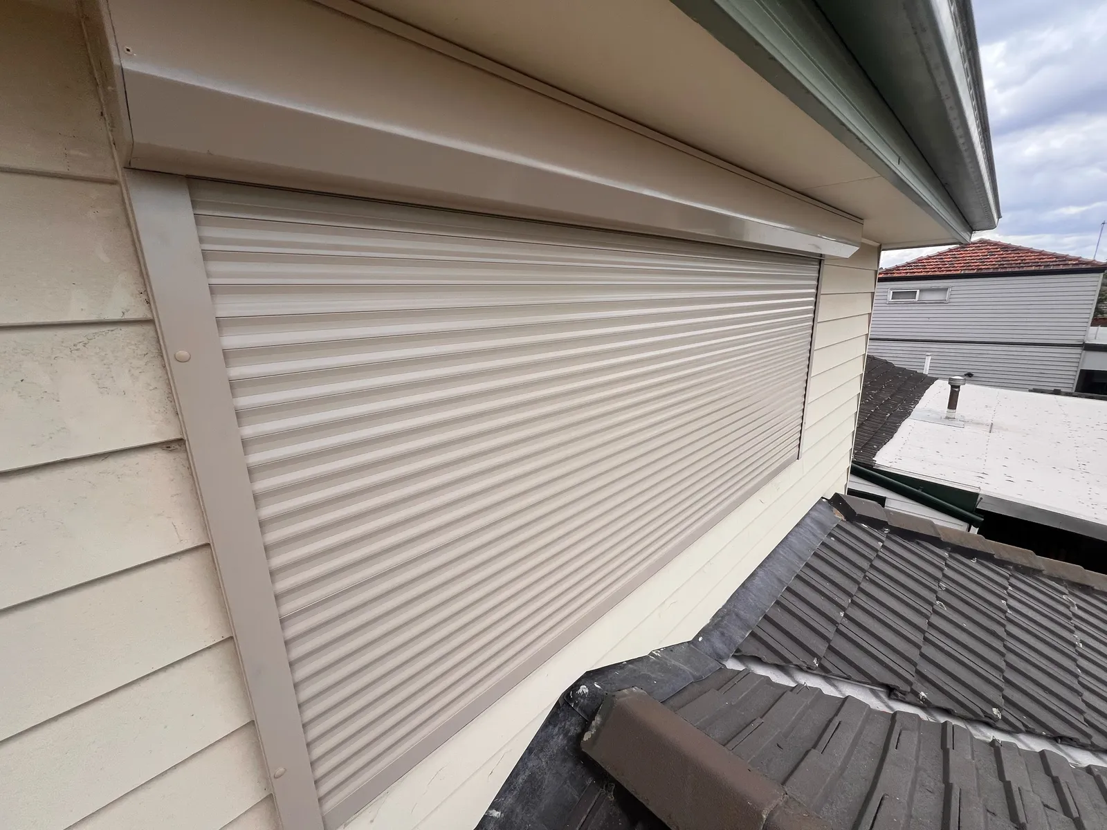 Close view of a light-coloured roller shutter and headbox on a weatherboard wall