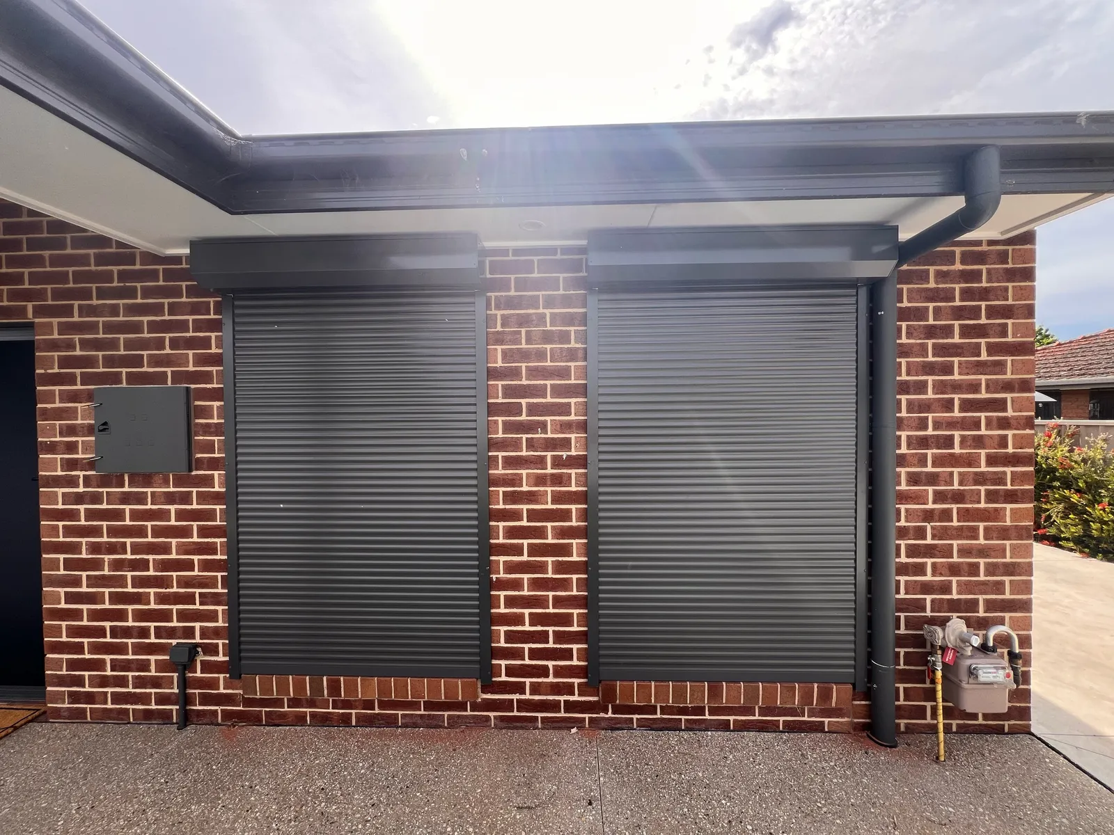 Two dark roller shutters on neighbouring windows of a red brick home