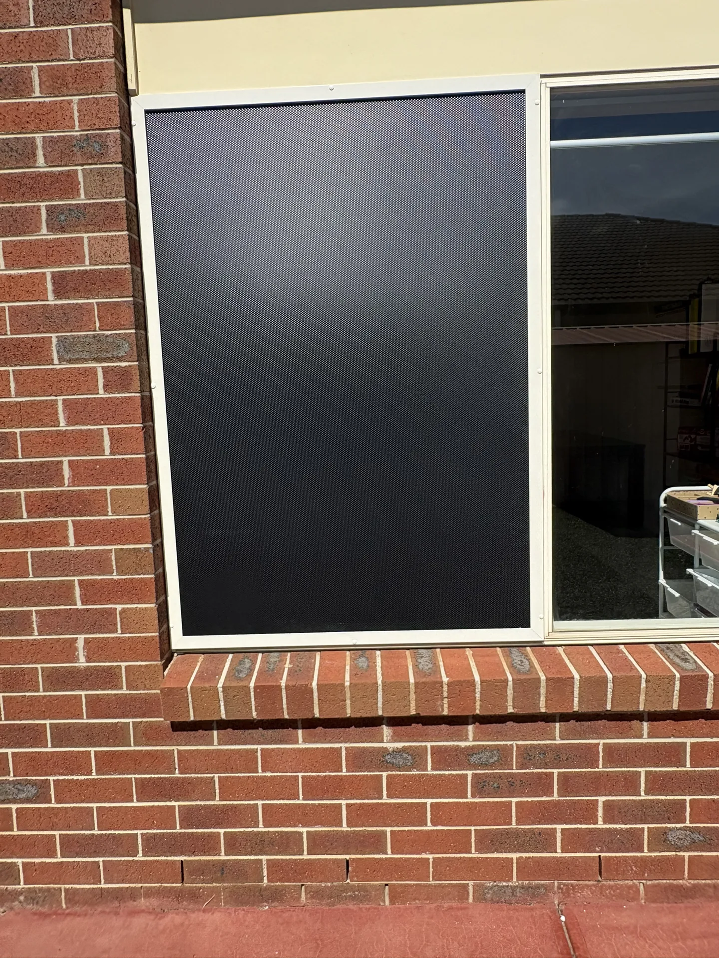 Security screen in a white frame covering a window beside a brick wall
