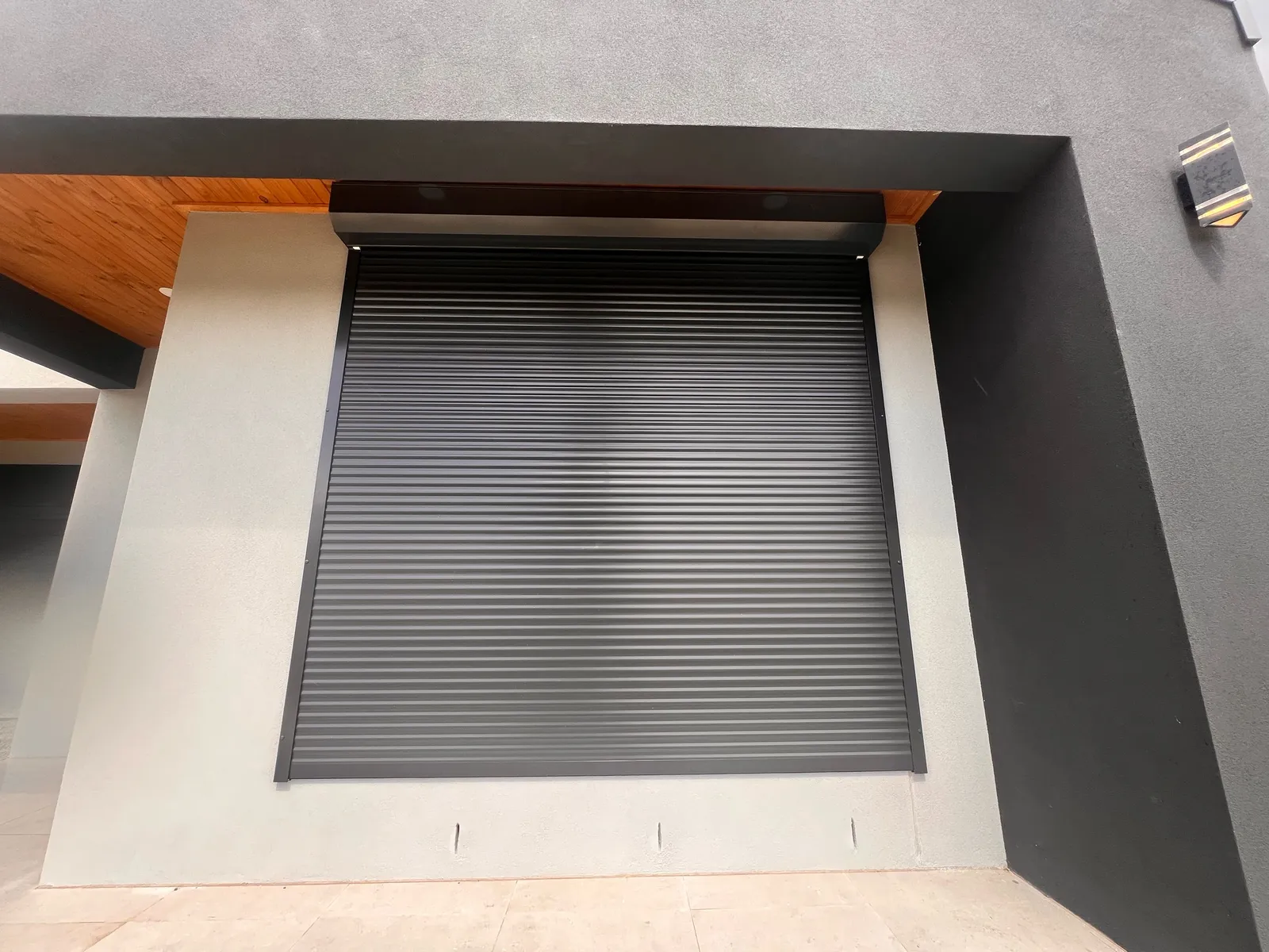 Dark roller shutter over a large opening on a modern rendered home