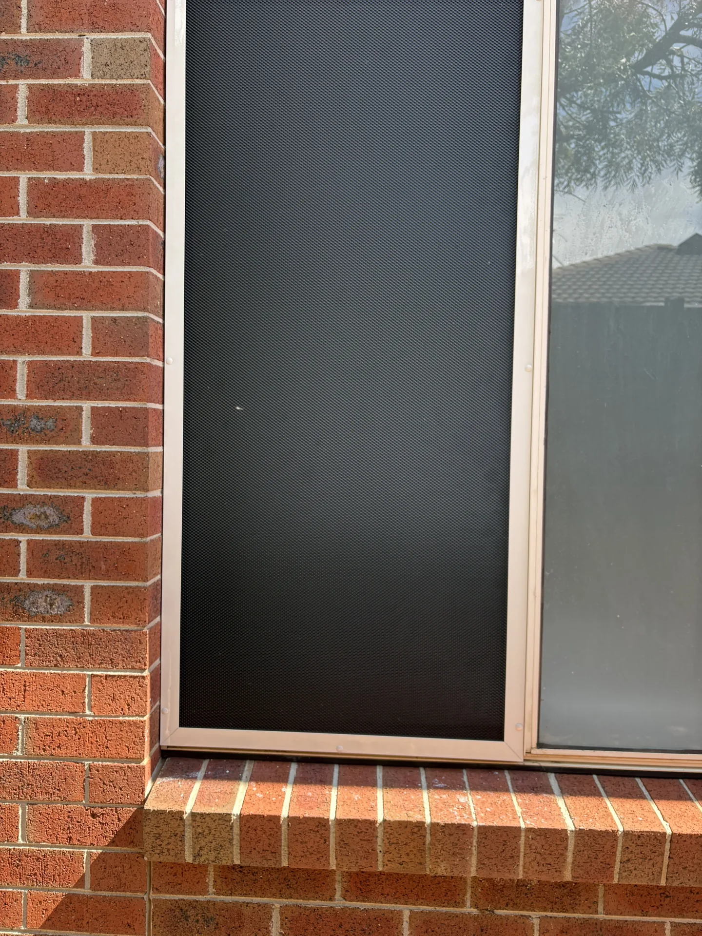 White-framed security screen fitted over a window on a brick home
