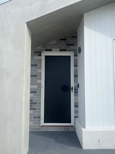 White-framed hinged security door with dark mesh at a front entry