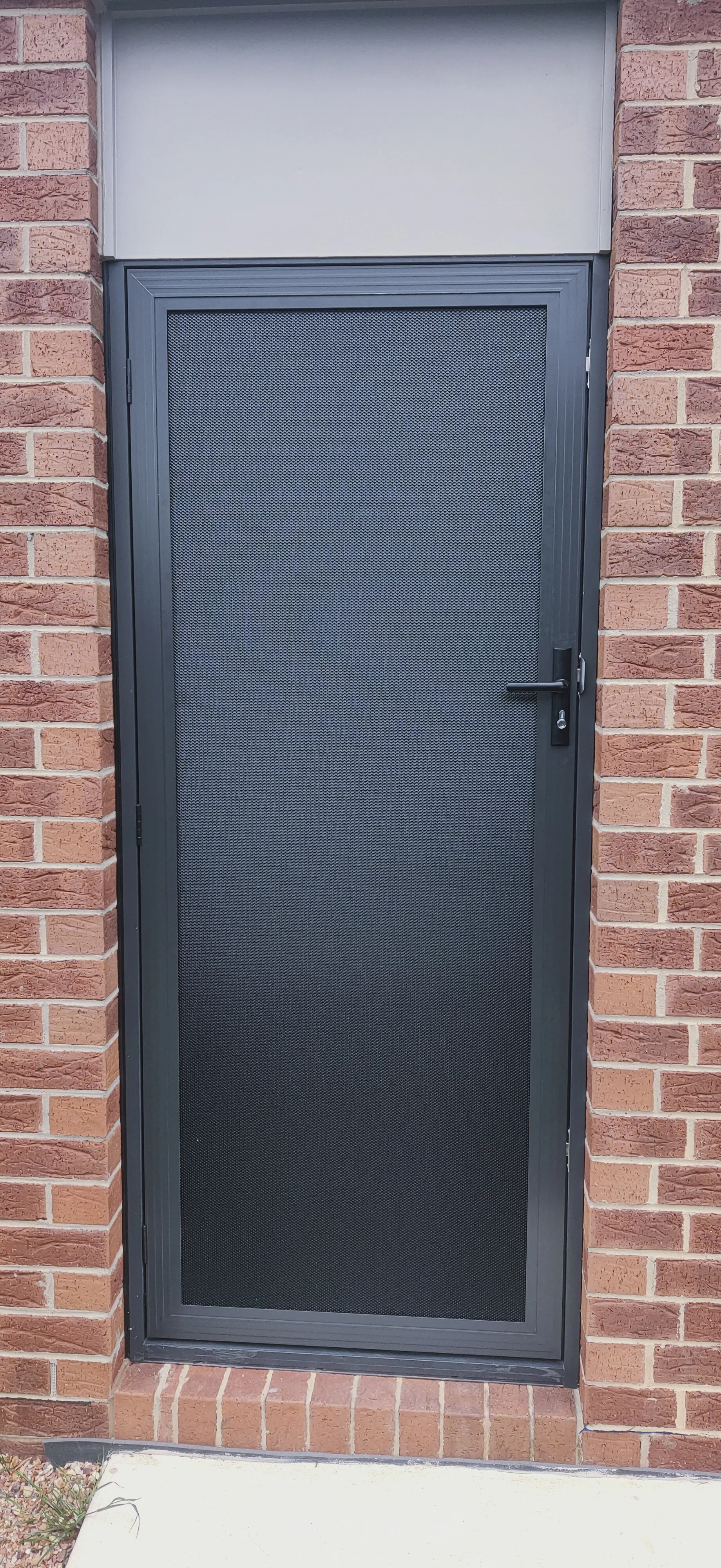 Black mesh security door fitted to a red brick home
