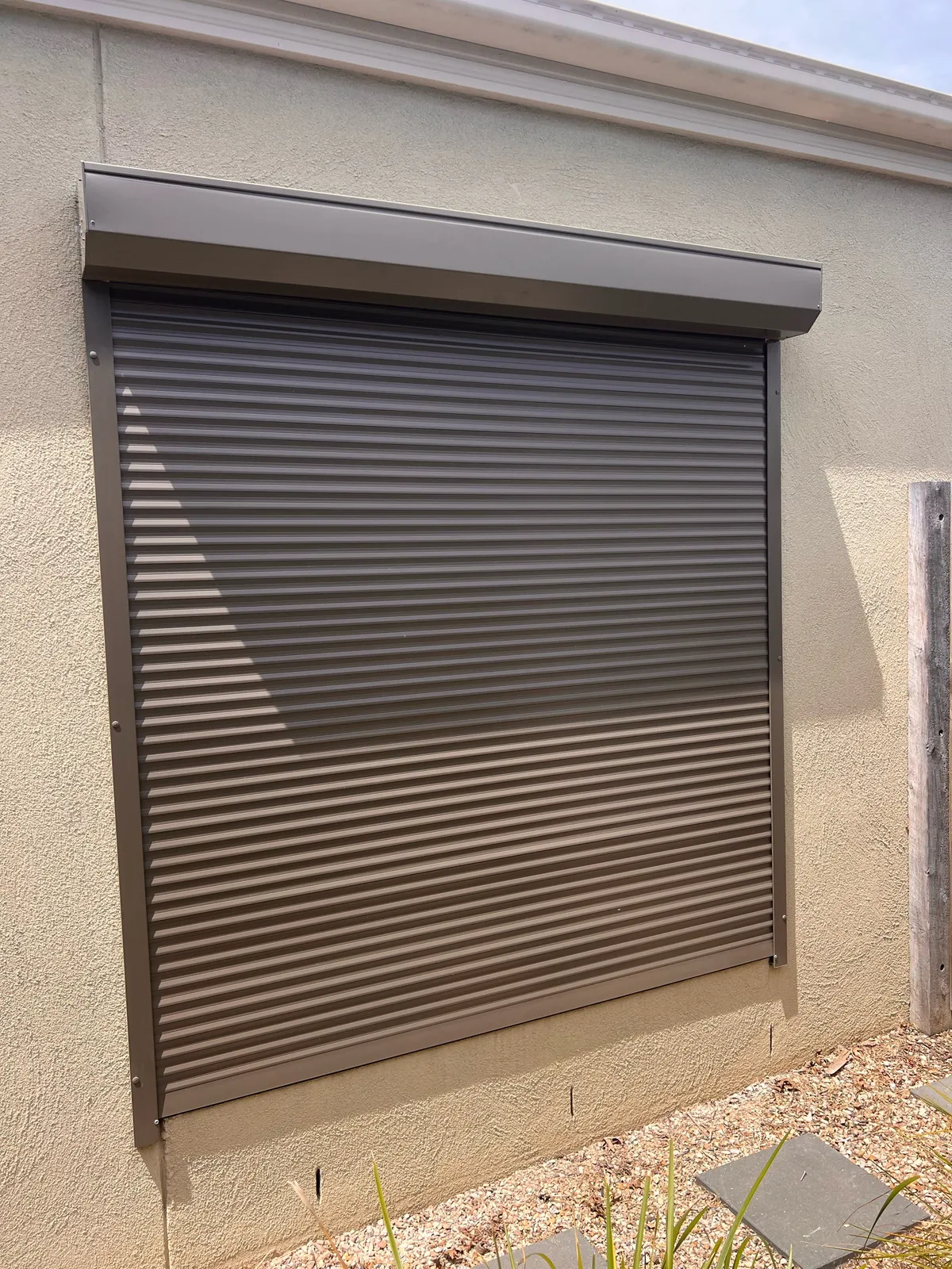 Dark roller shutter closed over a window on a cream rendered wall