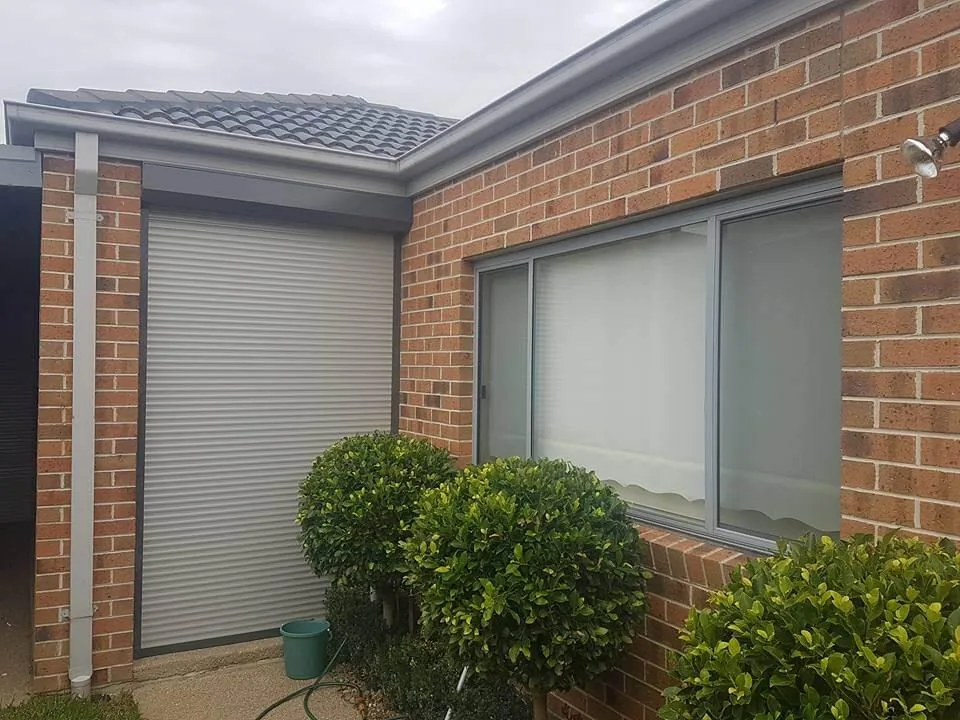 Residential roller shutter installed on a brick home beside a grey-framed window