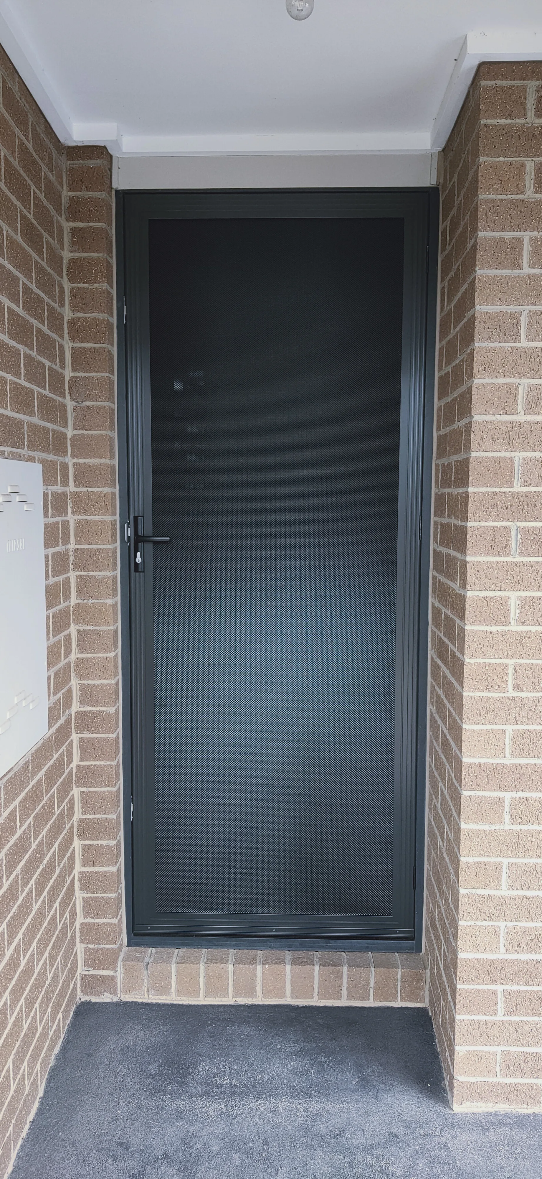 Black hinged security door with mesh infill installed at a brick home's entry porch