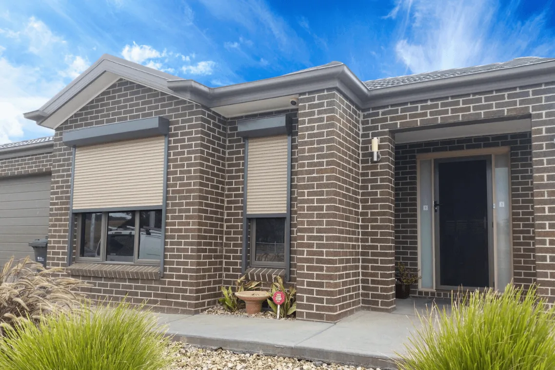 Completed roller shutter installation on the windows of a brick home